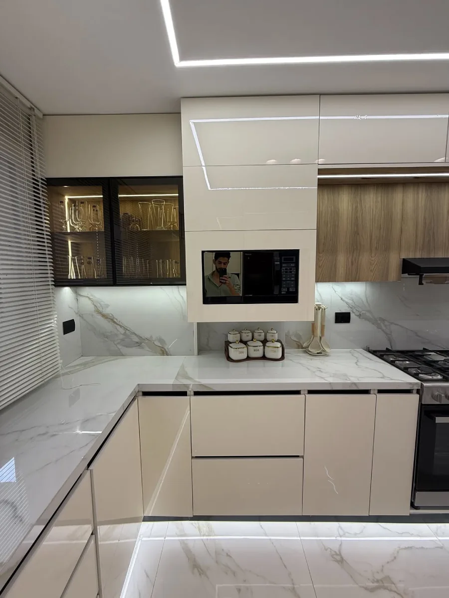 Detail lemari penyimpanan dapur warna krem high-gloss dengan rak kaca display dan microwave tanam yang rapi.