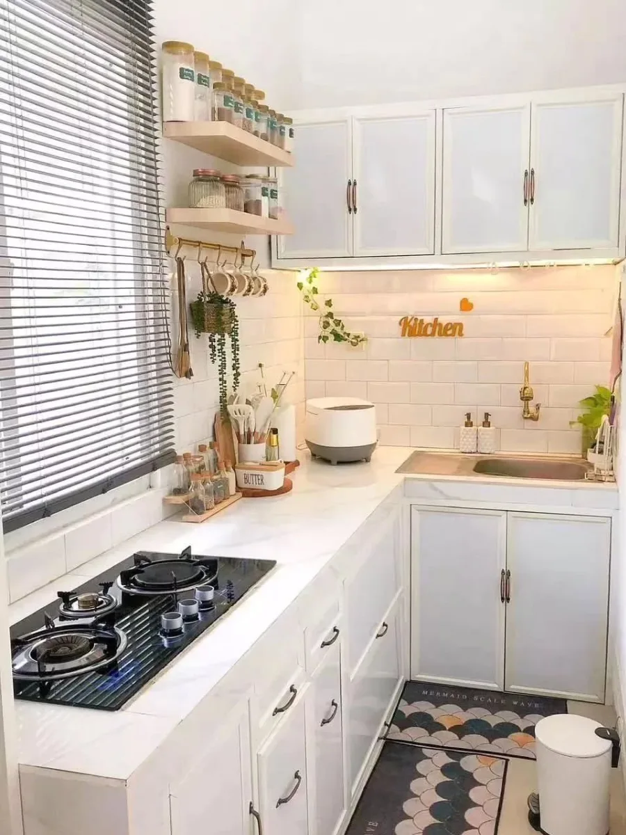 Pemanfaatan ruang sempit untuk dapur minimalis dengan jendela besar ber-blinds, rak bumbu dinding kayu estetik, dan kabinet bawah putih klasik.
