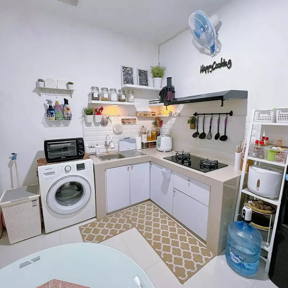 Desain dapur sudut minimalis multifungsi yang menyatu dengan area laundry (mesin cuci), dilengkapi wallpaper dinding bata putih dan rak bumbu dinding untuk menghemat ruang.