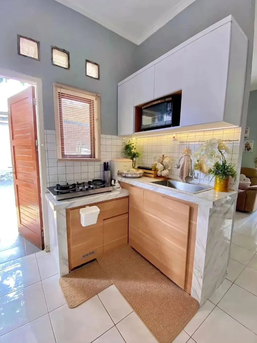 Inspirasi dapur minimalis di dekat pintu belakang dengan kombinasi kabinet bawah nuansa kayu natural, top table motif marmer, dan jendela nako untuk sirkulasi udara yang baik.