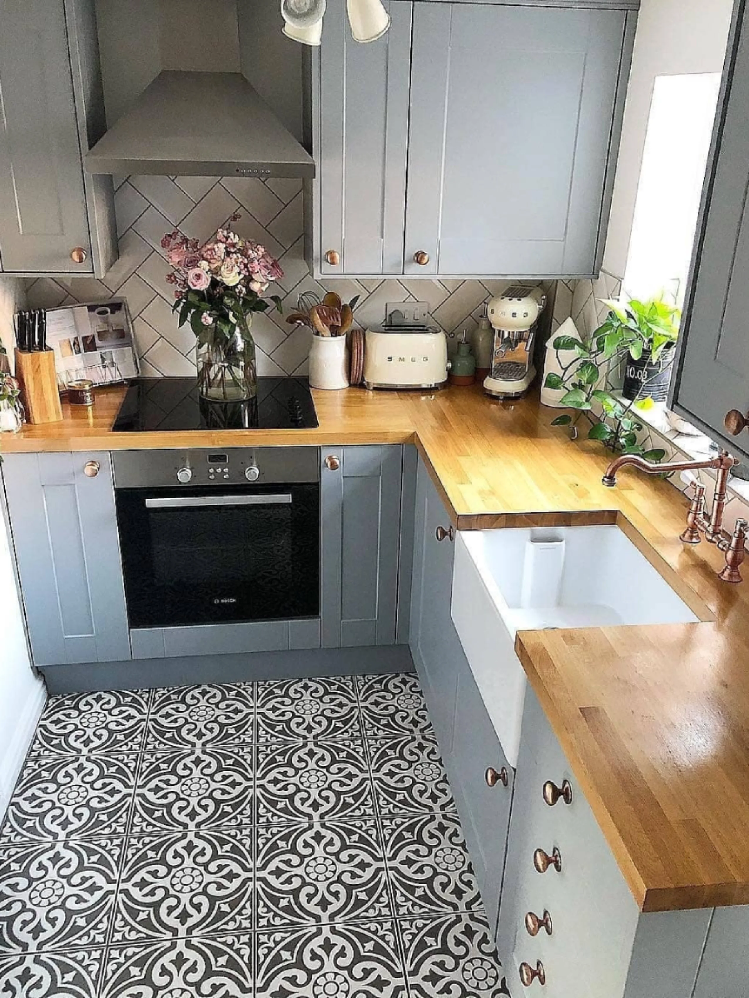 Interior dapur minimalis modern dengan sentuhan klasik (farmhouse), menampilkan kabinet abu-abu, lantai tegel motif vintage, keran tembaga, dan bak cuci piring keramik besar.