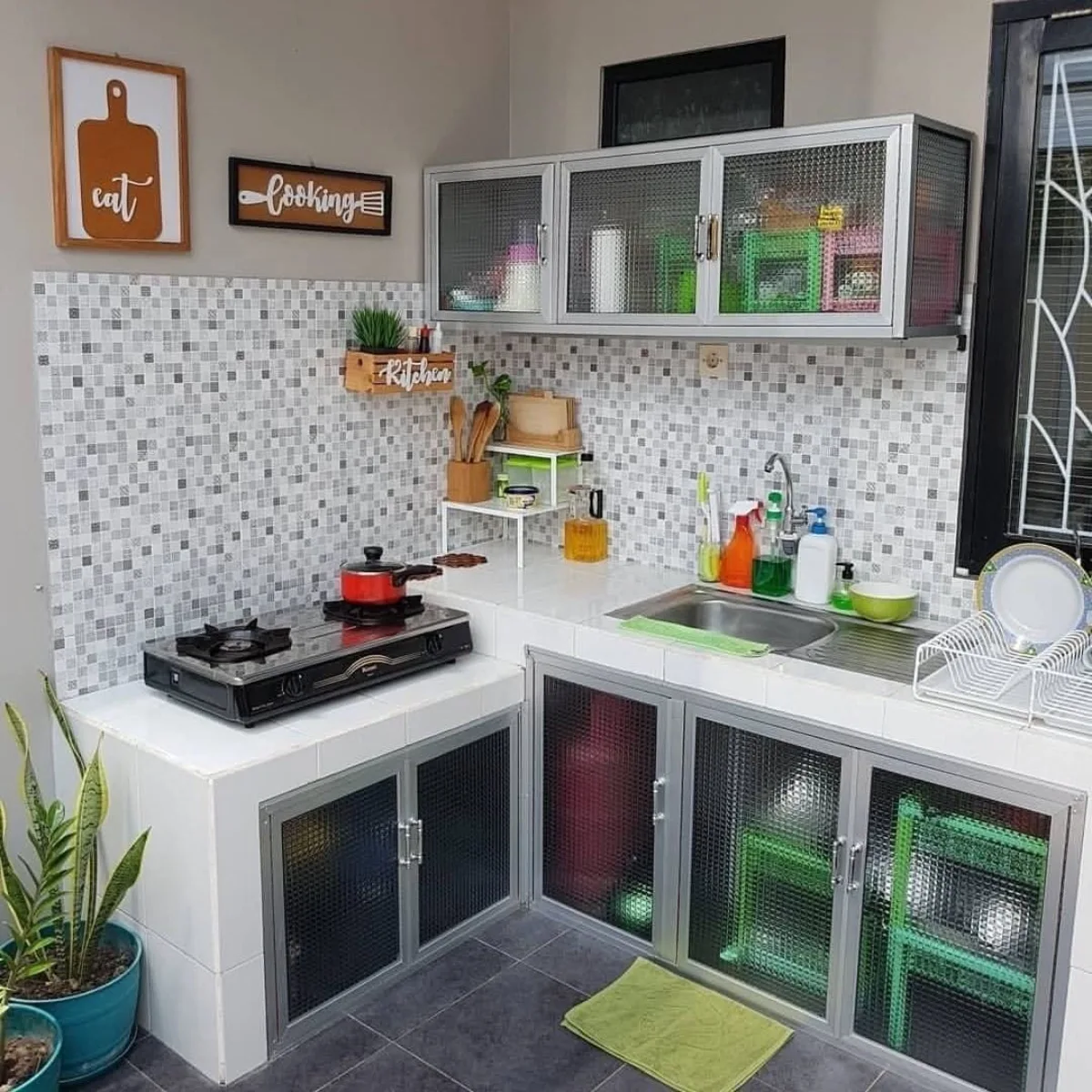 Model kitchen set aluminium kaca yang ekonomis dan anti rayap, dipadukan dengan dinding keramik mozaik abu-abu dan kompor gas portable untuk dapur sederhana.