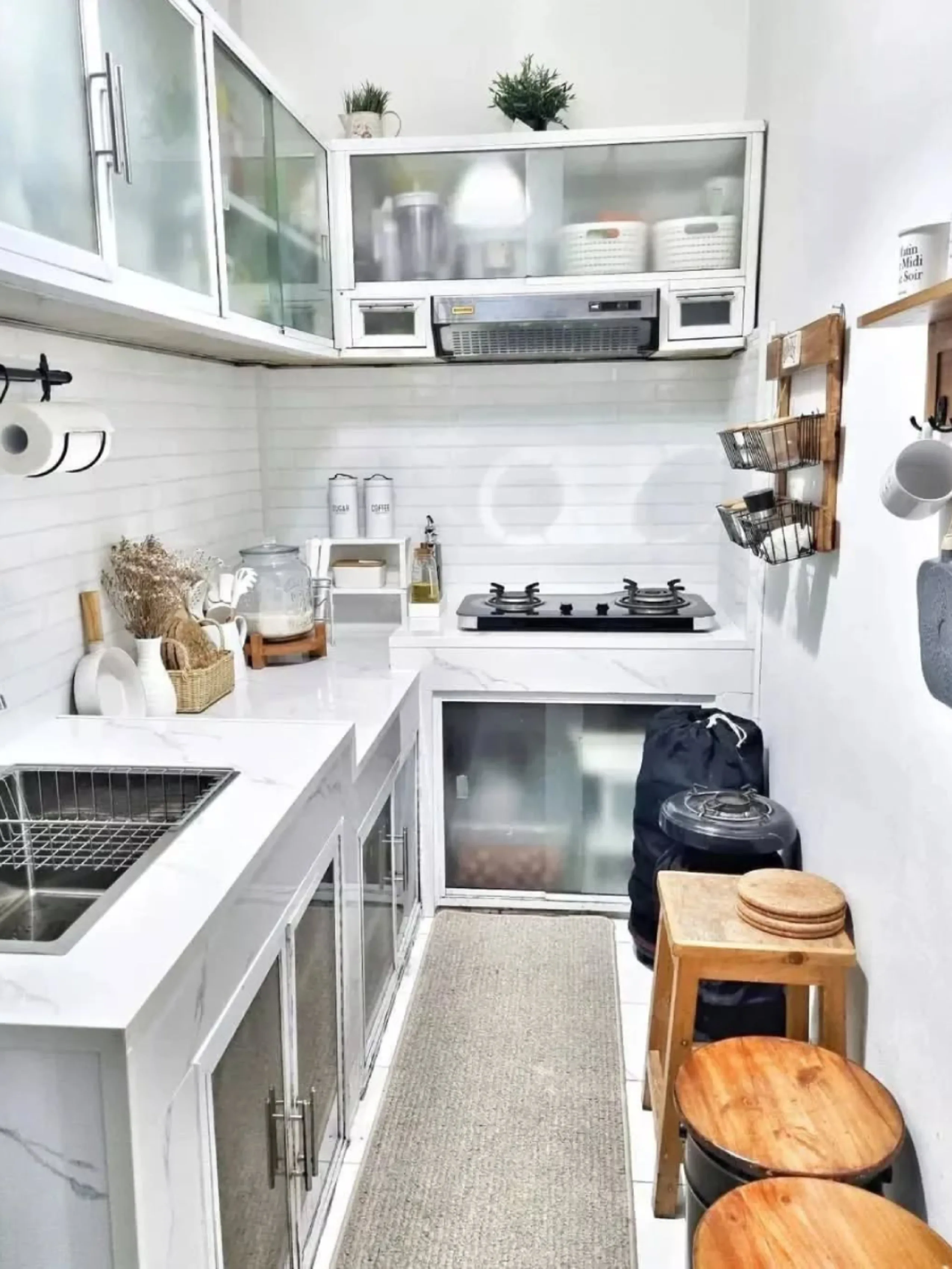 Solusi desain untuk dapur sangat sempit (lorong) dengan kabinet gantung kaca agar ruangan terasa lega, meja dapur marmer putih, dan kursi kayu bulat.
