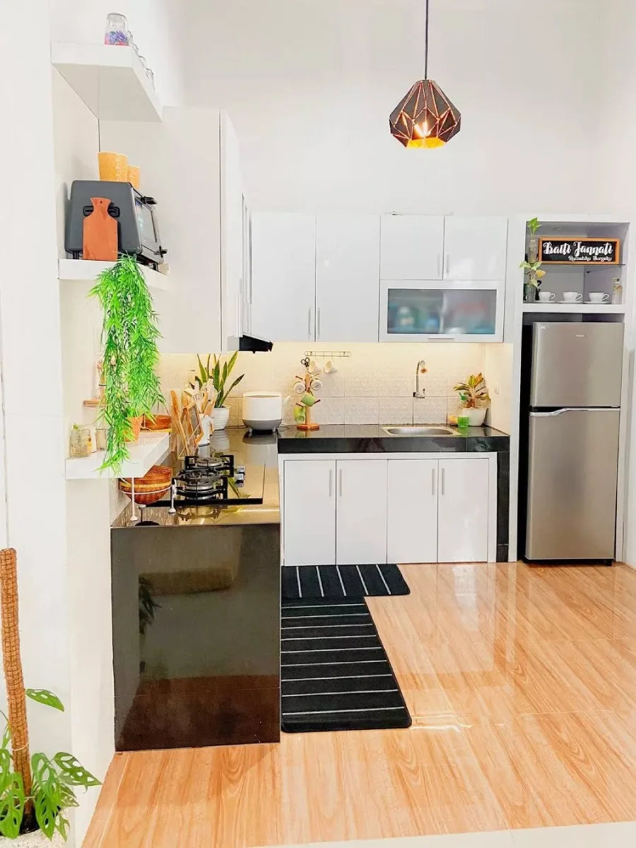 Layout dapur minimalis bentuk L dengan top table granit hitam yang kontras dengan kabinet putih glossy, serta lantai motif kayu yang memberikan kesan hangat.