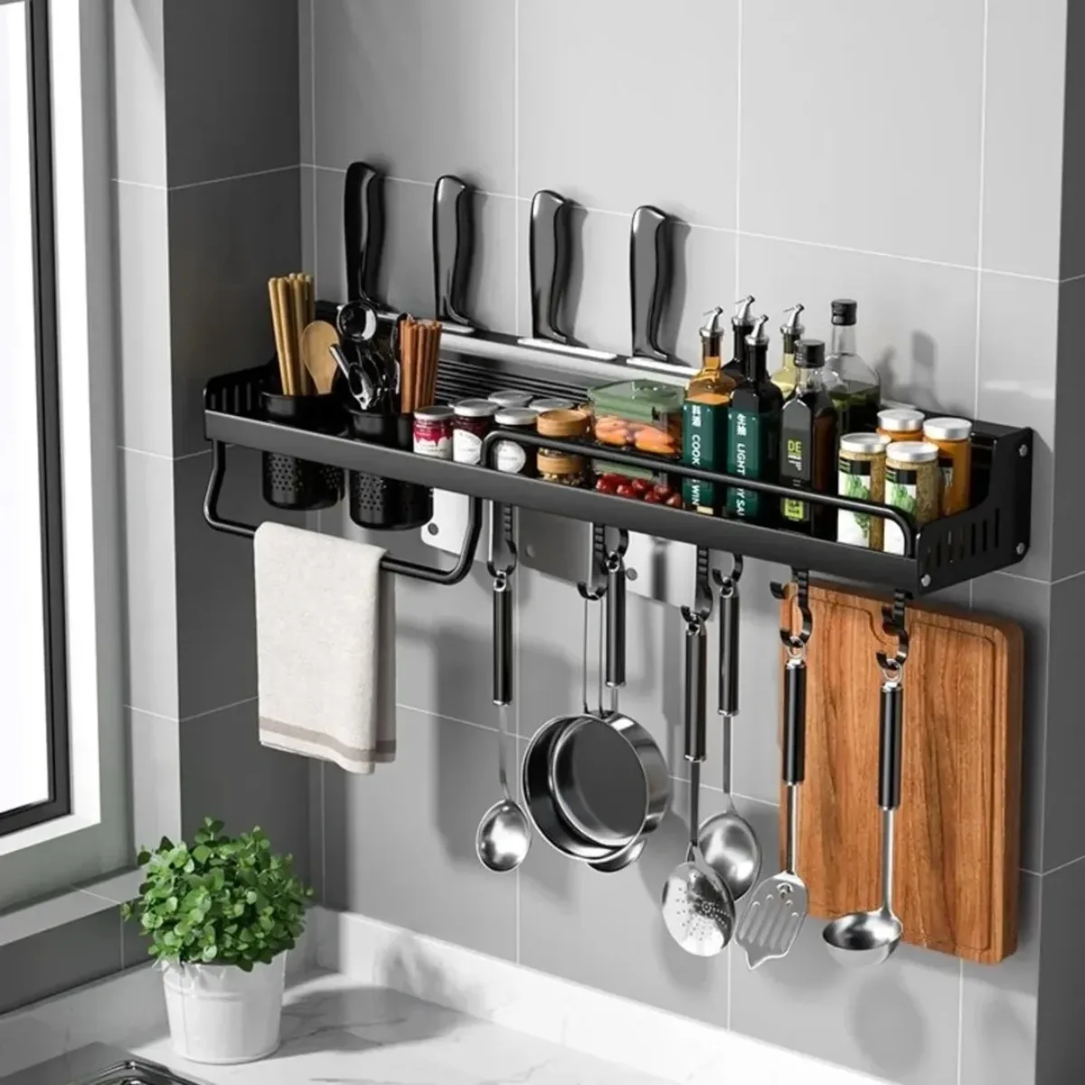 Rak dapur gantung berbahan besi hitam menempel di dinding keramik berisi koleksi pisau, botol bumbu, talenan, dan panci yang digantung