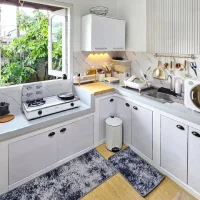 Dapur minimalis dengan jendela besar menghadap taman hijau untuk pencahayaan alami, kabinet putih sederhana, dan area cuci piring yang terang.