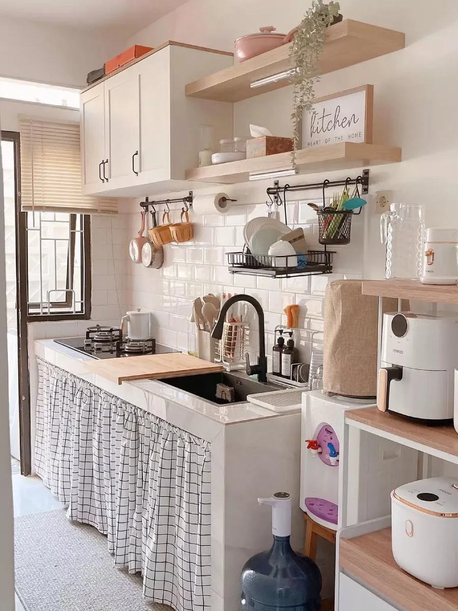 Dapur kecil bergaya Skandinavia dengan kabinet putih gantung, rak kayu terbuka, backsplash subway tile putih, dan tirai kolong dapur motif kotak-kotak.