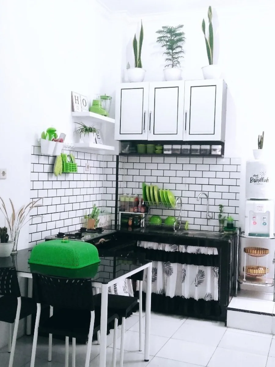 Sudut dapur kecil minimalis dengan tema hitam putih yang kontras, rak dinding ambalan untuk toples bumbu, dan tirai kolong dapur motif daun tropis.