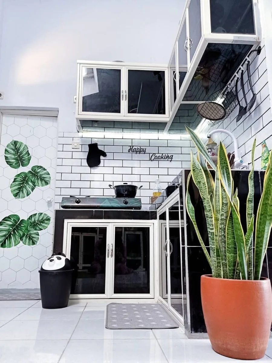 Dapur mungil tema monokrom hitam putih dengan kabinet aluminium kaca, dinding keramik bata putih, dan dekorasi stiker dinding motif daun monstera yang hemat biaya.