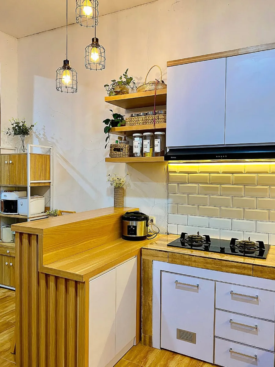 Dapur dengan lampu gantung sangkar besi gaya industrial, rak ambalan kayu terbuka, backsplash keramik bata krem, dan kombinasi kabinet putih dengan aksen kayu.