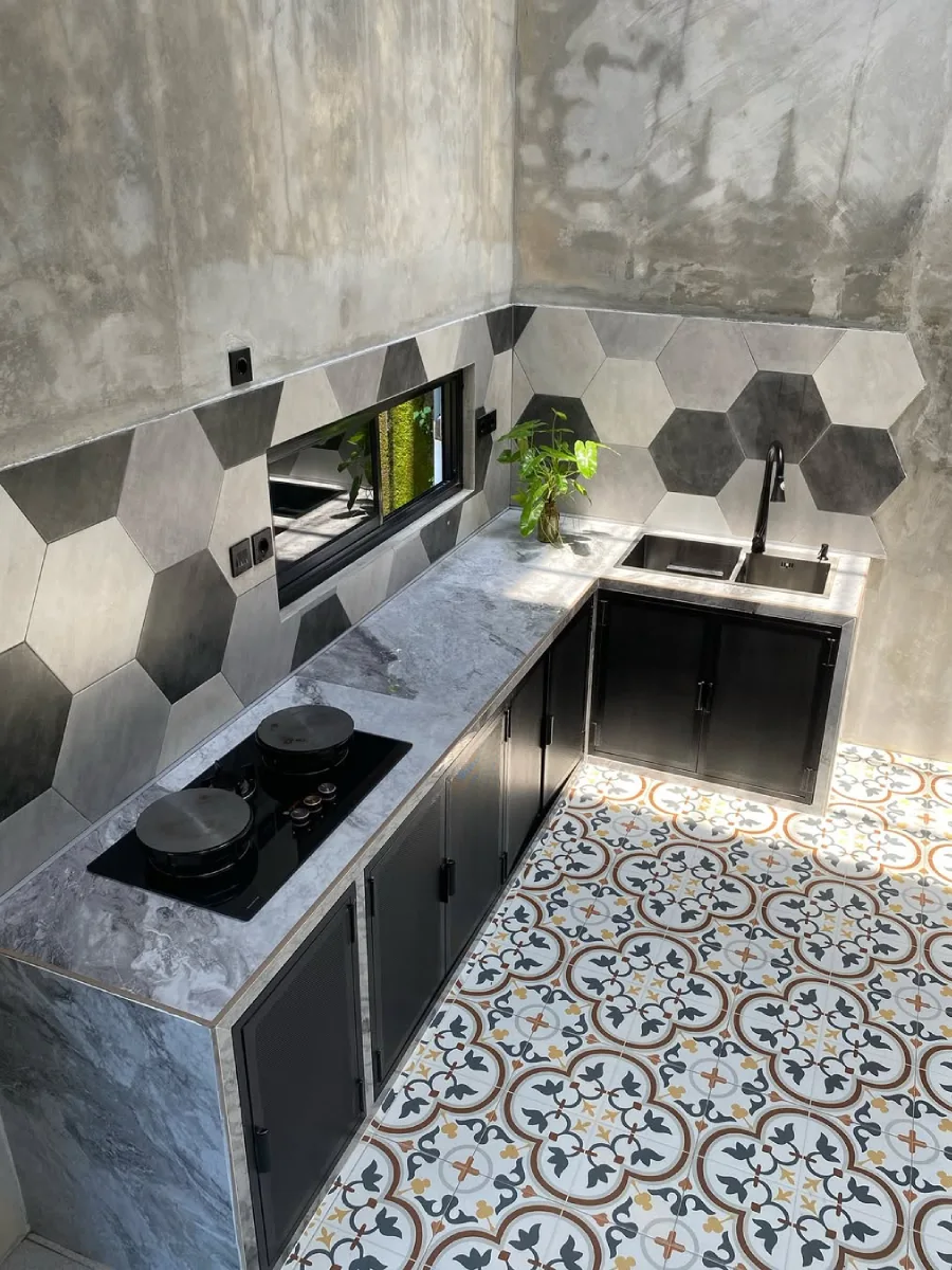 Desain dapur bergaya industrial dengan dinding beton ekspos, keramik dinding heksagonal warna monokrom, kabinet bawah hitam, dan lantai tegel motif klasik.