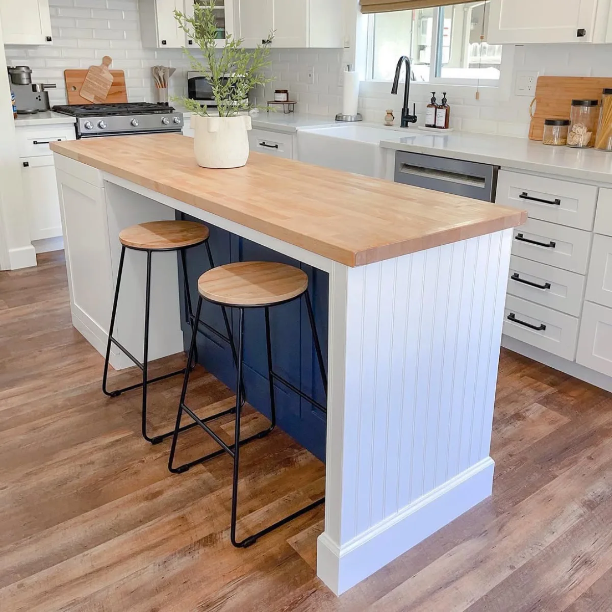 Meja kitchen island bergaya klasik dengan permukaan kayu solid tebal dan panel dasar berwarna putih dan biru gelap dilengkapi dua kursi bar kayu