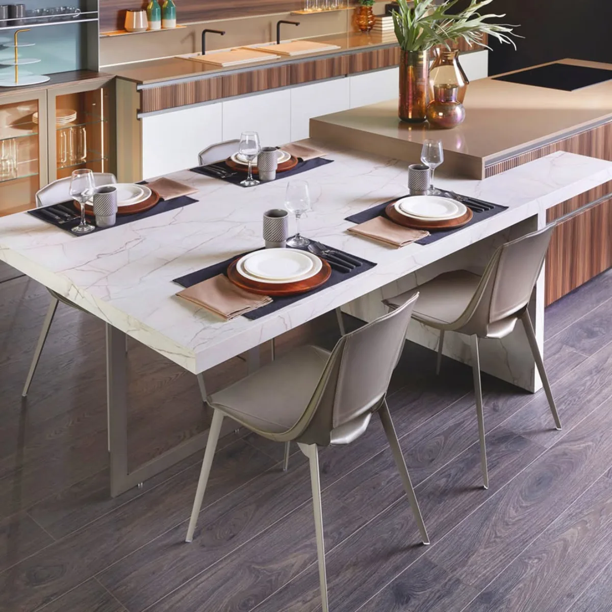 Meja makan berpermukaan marmer putih elegan yang menyatu dengan kitchen island modern dan dikelilingi kursi makan kulit abu-abu