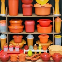 Rak berisi berbagai peralatan dapur plastik warna oranye dan kuning seperti wadah makanan, saringan, dan alat ukur tersusun rapi