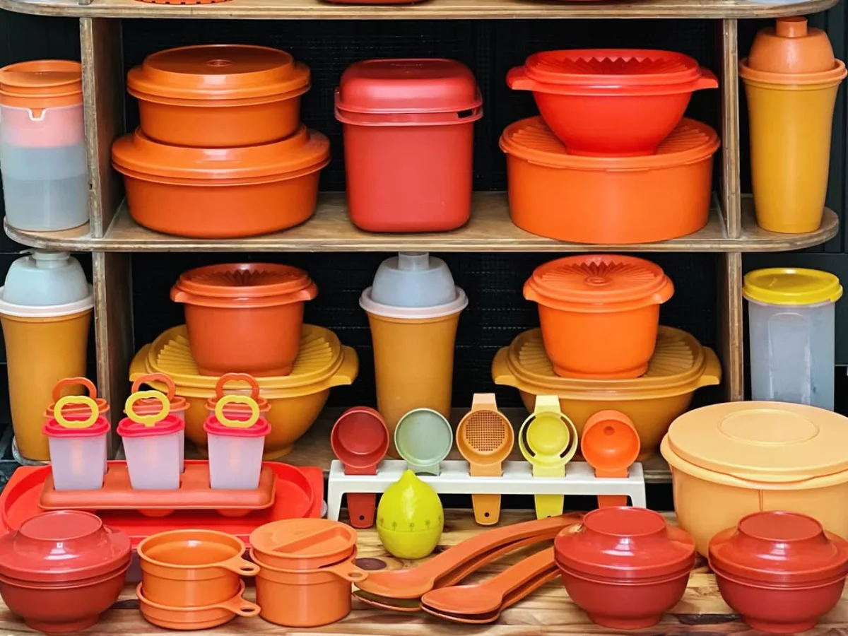 Rak berisi berbagai peralatan dapur plastik warna oranye dan kuning seperti wadah makanan, saringan, dan alat ukur tersusun rapi