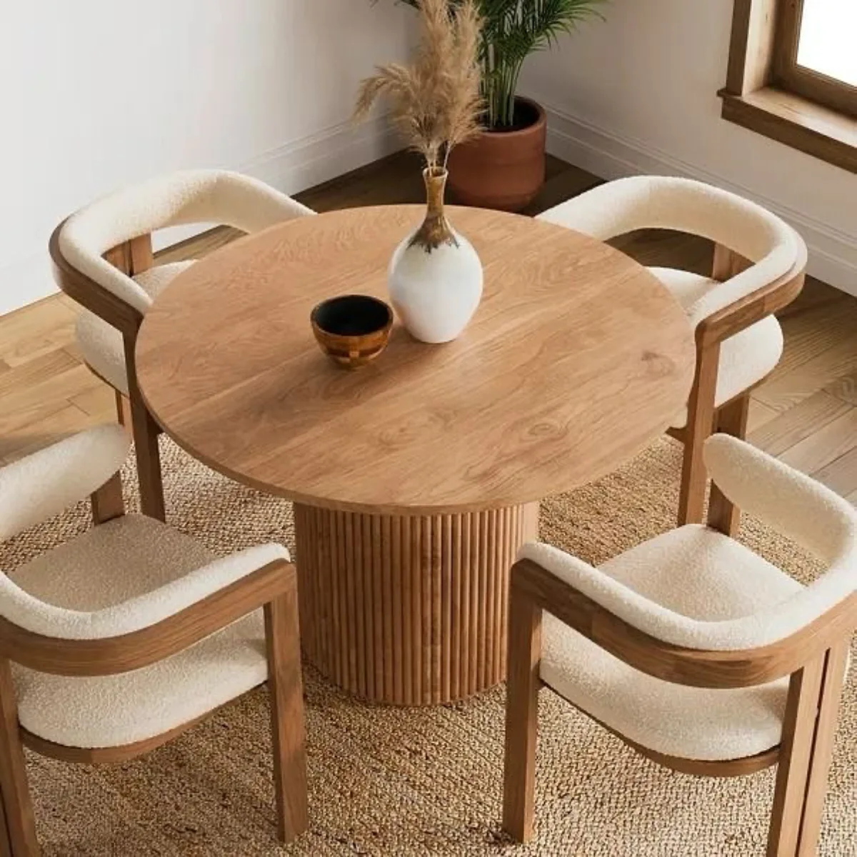 Set meja makan bundar bergaya Japandi dengan kaki kayu silinder bergaris dan empat kursi beraksen kayu lengkung dengan dudukan putih empuk.