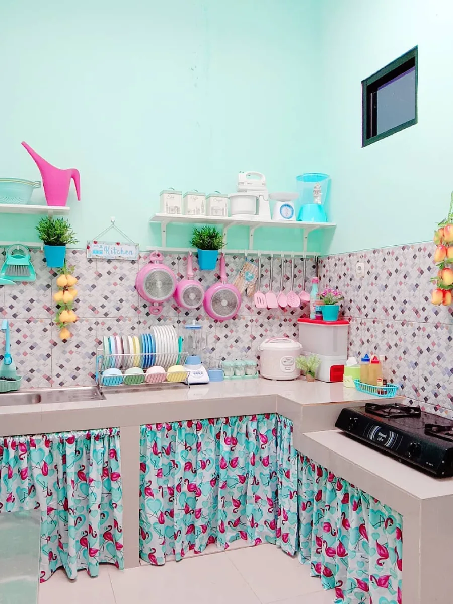 Detail dapur bernuansa ceria dengan cat dinding aqua blue, tirai kolong motif flamingo, serta perabotan memasak berwarna pink dan biru pastel.