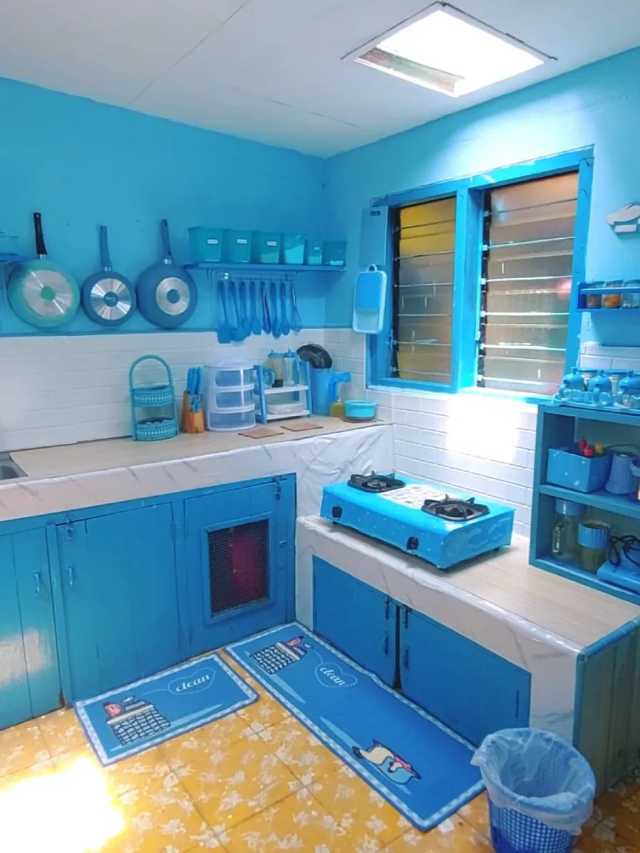 Dapur leter L dengan konsep monokromatik biru terang (electric cyan) pada dinding dan kabinet, dipadukan dengan lantai keramik kuning bermotif.