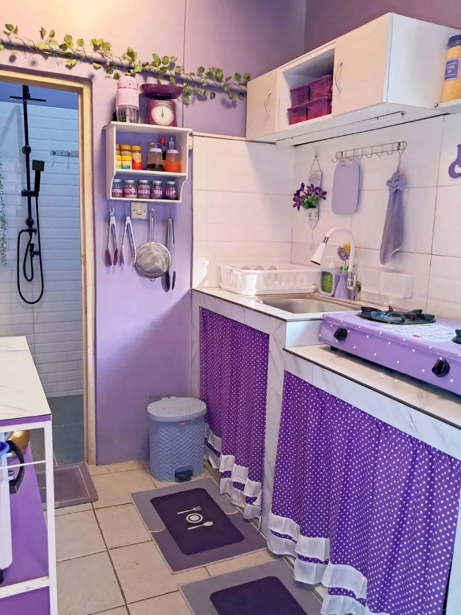 Inspirasi dapur sempit menyatu dengan area kamar mandi, menggunakan cat dinding ungu lavender dan penataan rak dinding vertikal.