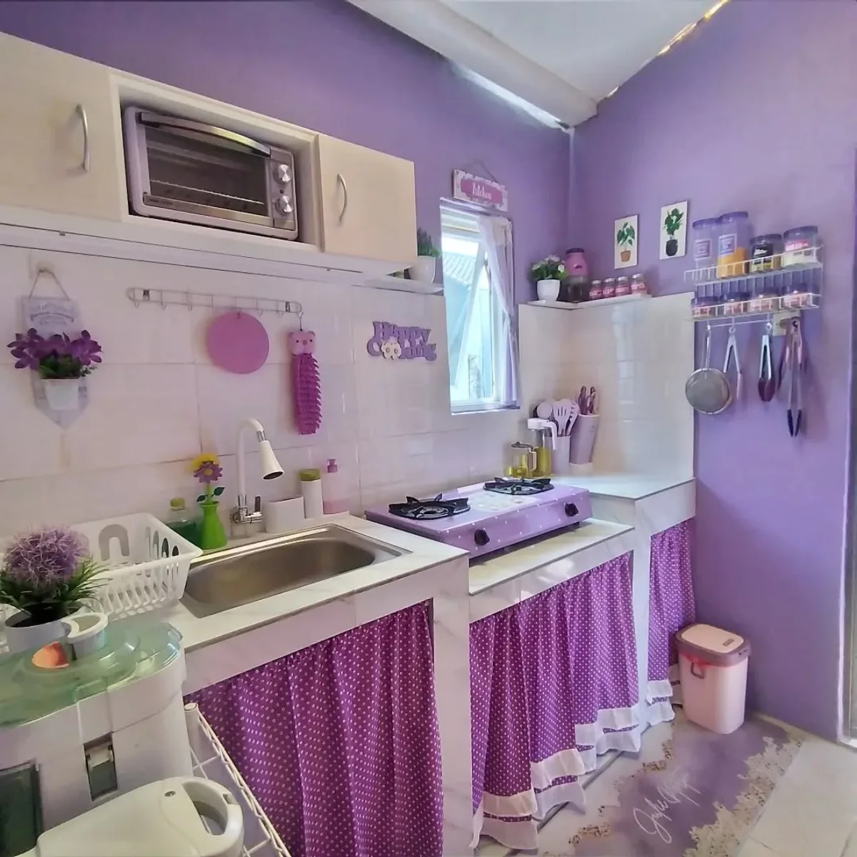 Dapur sederhana nuansa ungu lengkap dengan microwave di kabinet atas dan tempat sampah estetik berwarna senada.