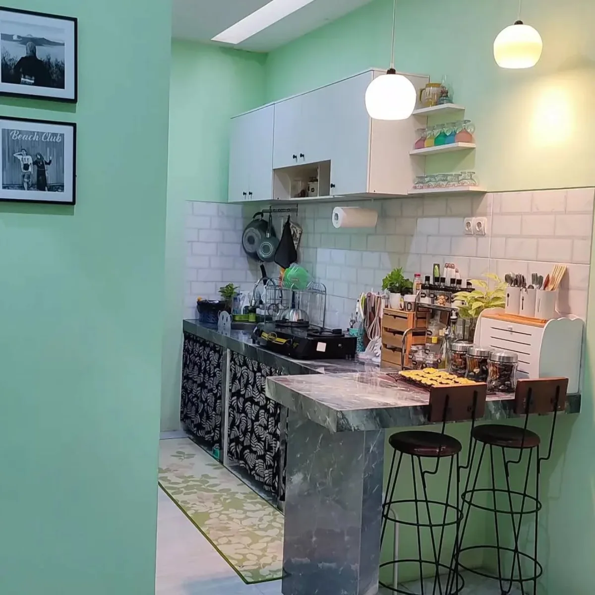 Interior dapur minimalis modern dengan cat dinding warna hijau mint sejuk (cool mint), meja bar marmer abu-abu, lampu gantung bulat estetik, dan rak dinding putih.