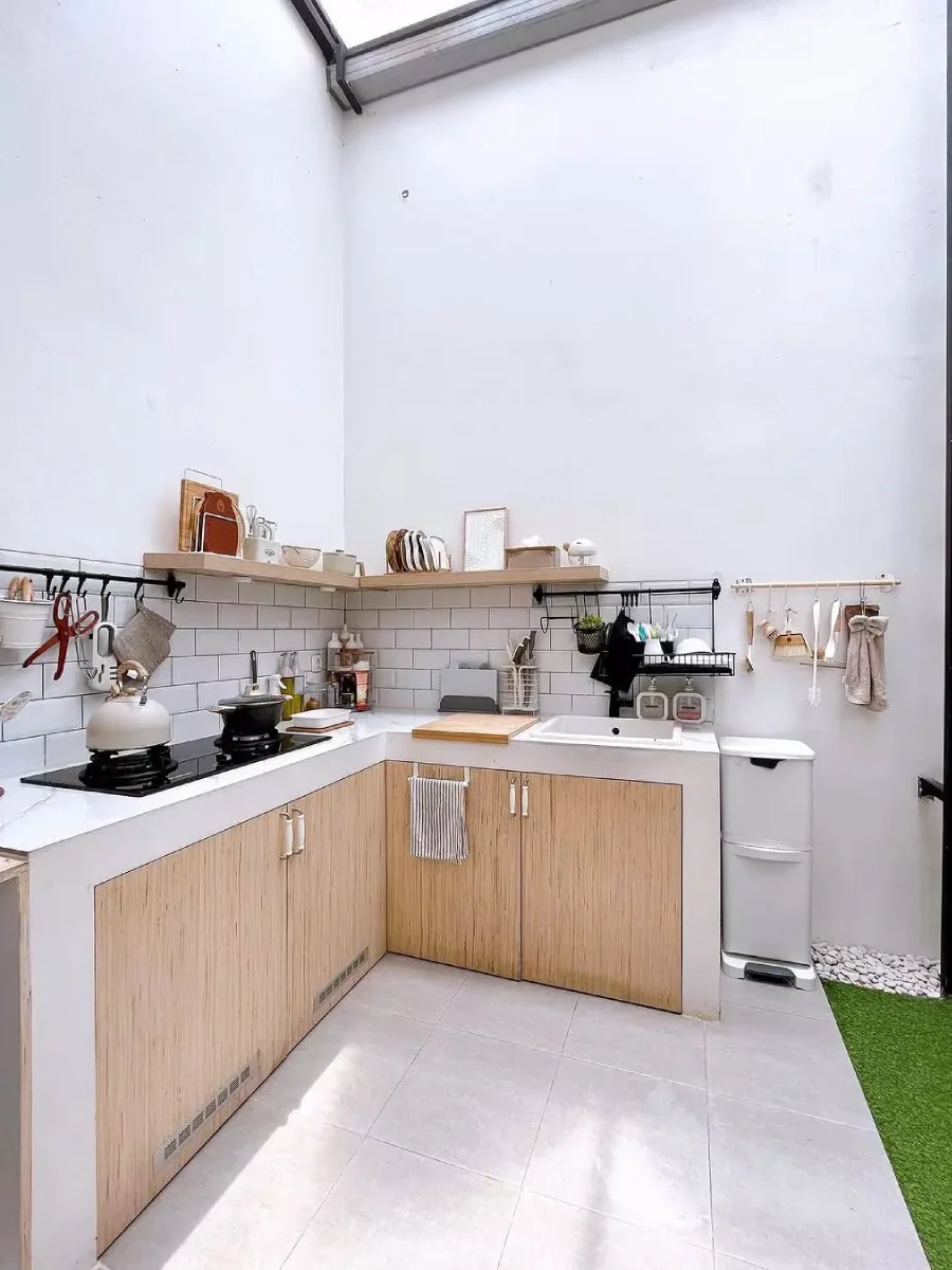 Inspirasi dapur semi-outdoor atap kaca (skylight) dengan dinding putih tinggi, kabinet bawah aksen kayu, dan lantai keramik abu-abu.