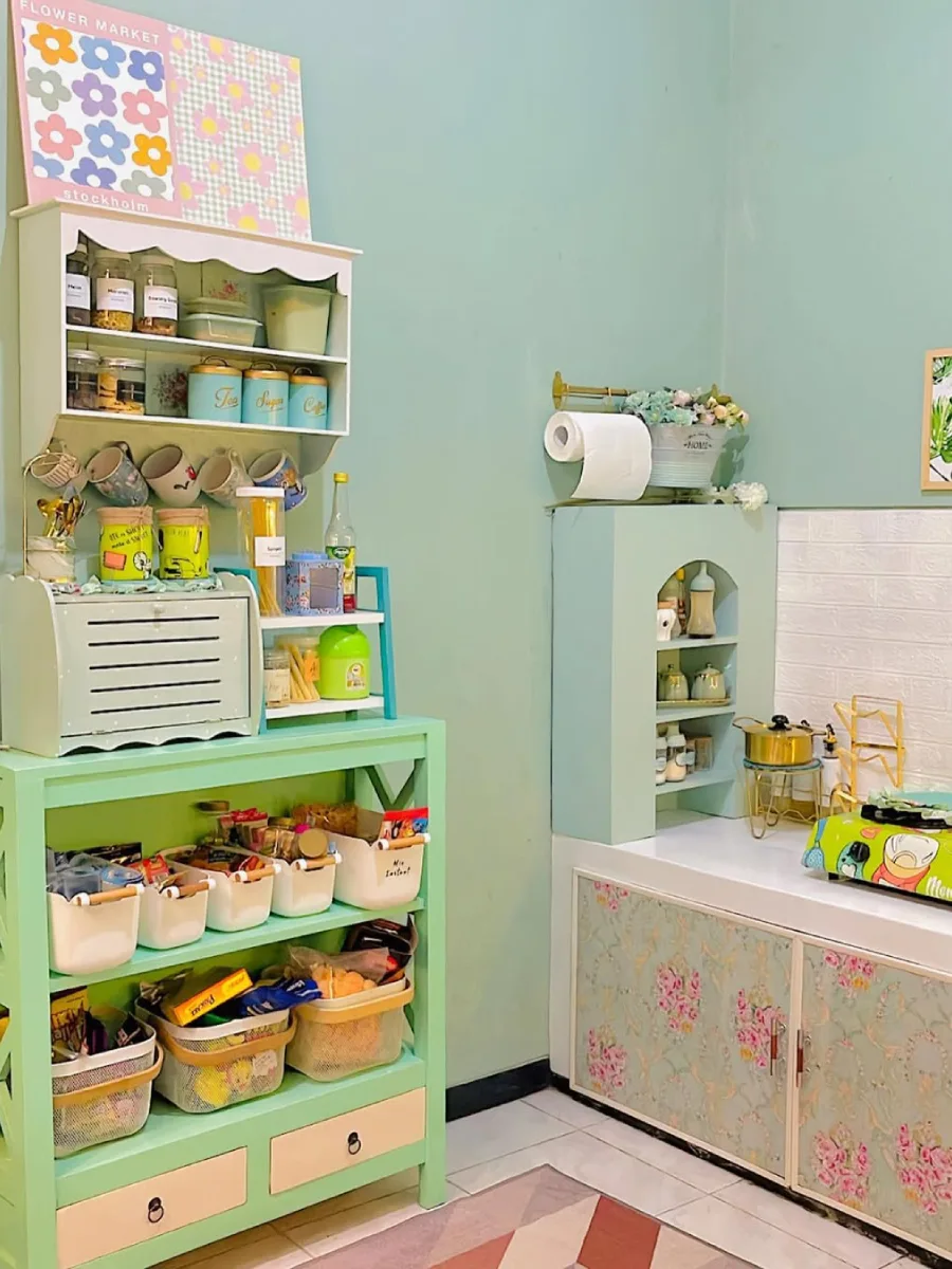 Sudut penyimpanan dapur dengan rak kayu cat hijau mint pastel, toples bumbu rapi, dan dekorasi dinding nuansa ceria.