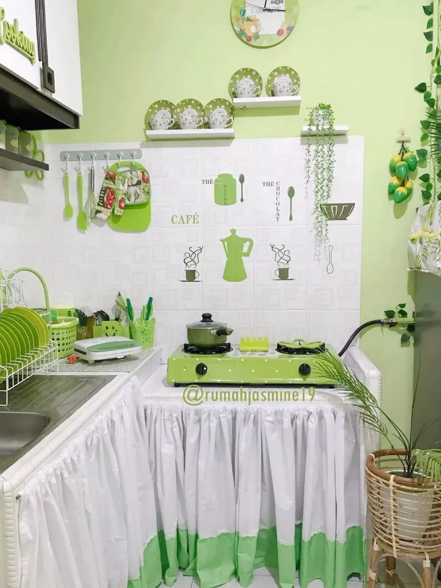 Area memasak dengan kompor gas hijau, dinding keramik putih dengan stiker dekoratif, dan cat dinding atas warna hijau pupus (spring green) yang segar.