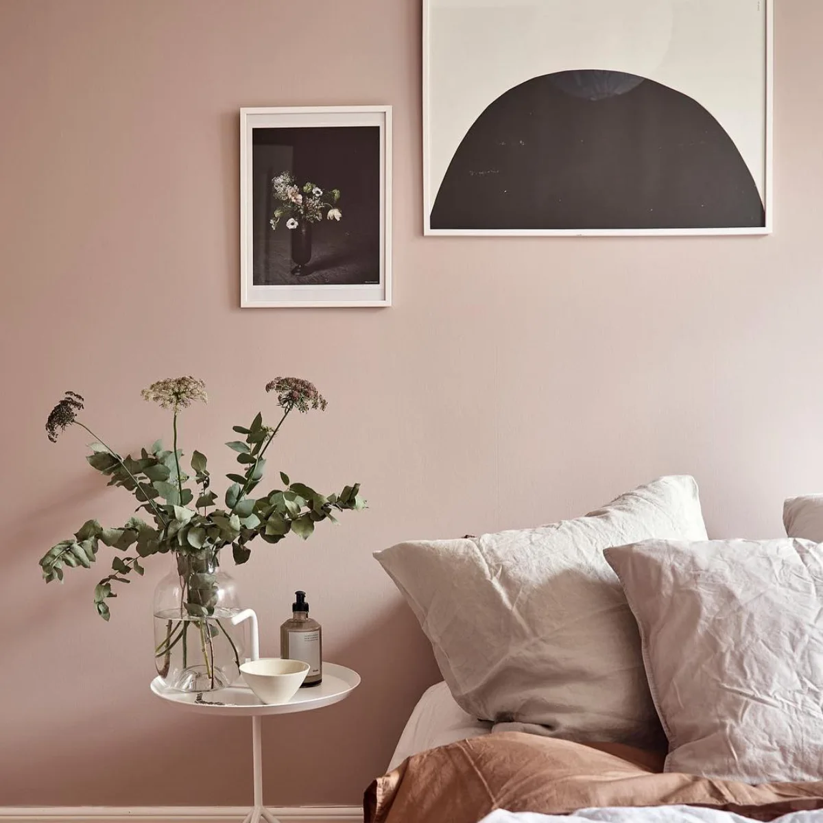 Kamar tidur estetik dengan cat dinding warna dusty pink atau merah muda pudar, dilengkapi dekorasi lukisan abstrak hitam putih dan tanaman hias minimalis.