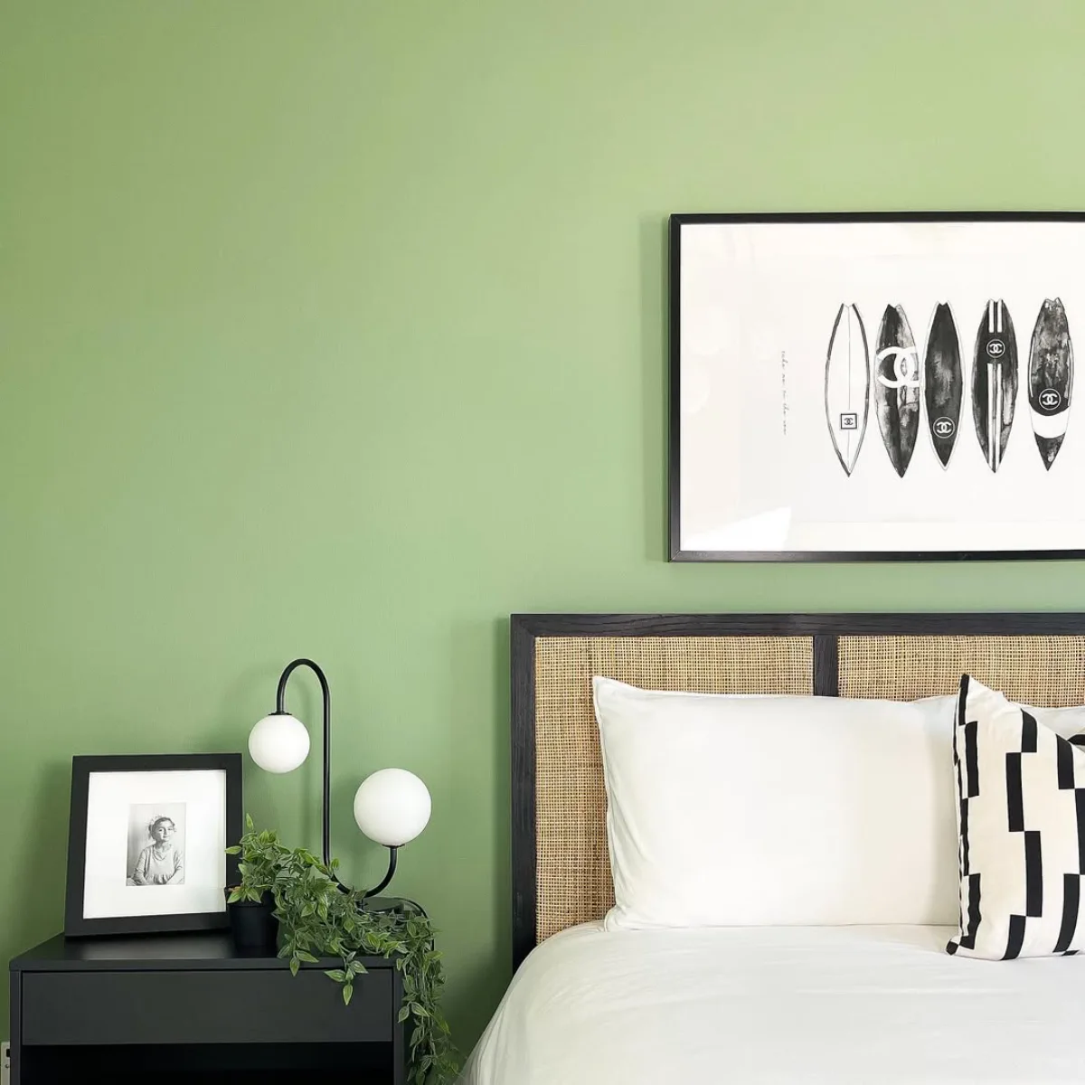 Inspirasi cat kamar tidur warna hijau sage yang segar dikombinasikan dengan sandaran kepala kasur (headboard) rotan dan nakas hitam modern.