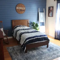 Kamar anak laki-laki dengan dinding biru navy, tempat tidur kayu, dan dekorasi sederhana yang modern dan hangat.