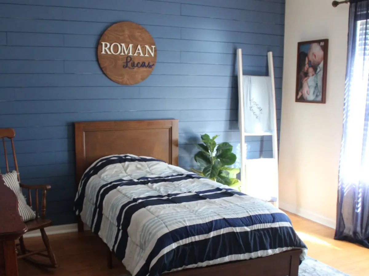 Kamar anak laki-laki dengan dinding biru navy, tempat tidur kayu, dan dekorasi sederhana yang modern dan hangat.