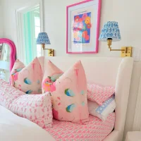 Kamar anak perempuan dengan dekorasi warna pink cerah, bantal motif abstrak, dan lampu dinding biru bermotif etnik.