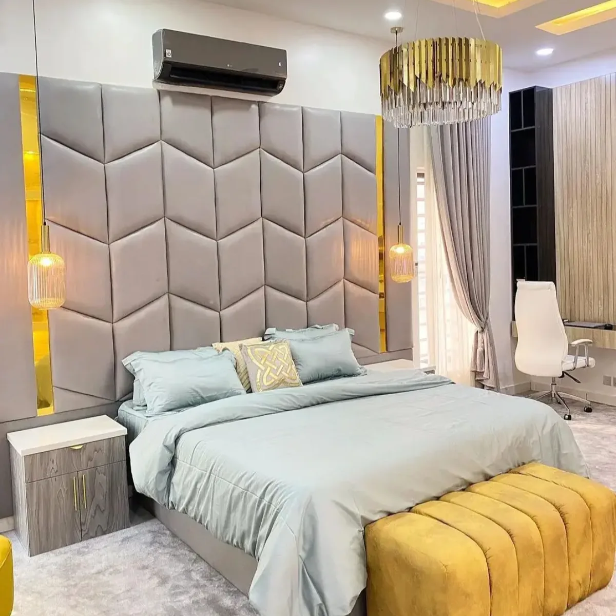 Panel headboard geometris berlapis abu-abu besar yang menutupi dinding di atas tempat tidur besar di kamar tidur modern, diapit oleh lampu gantung.