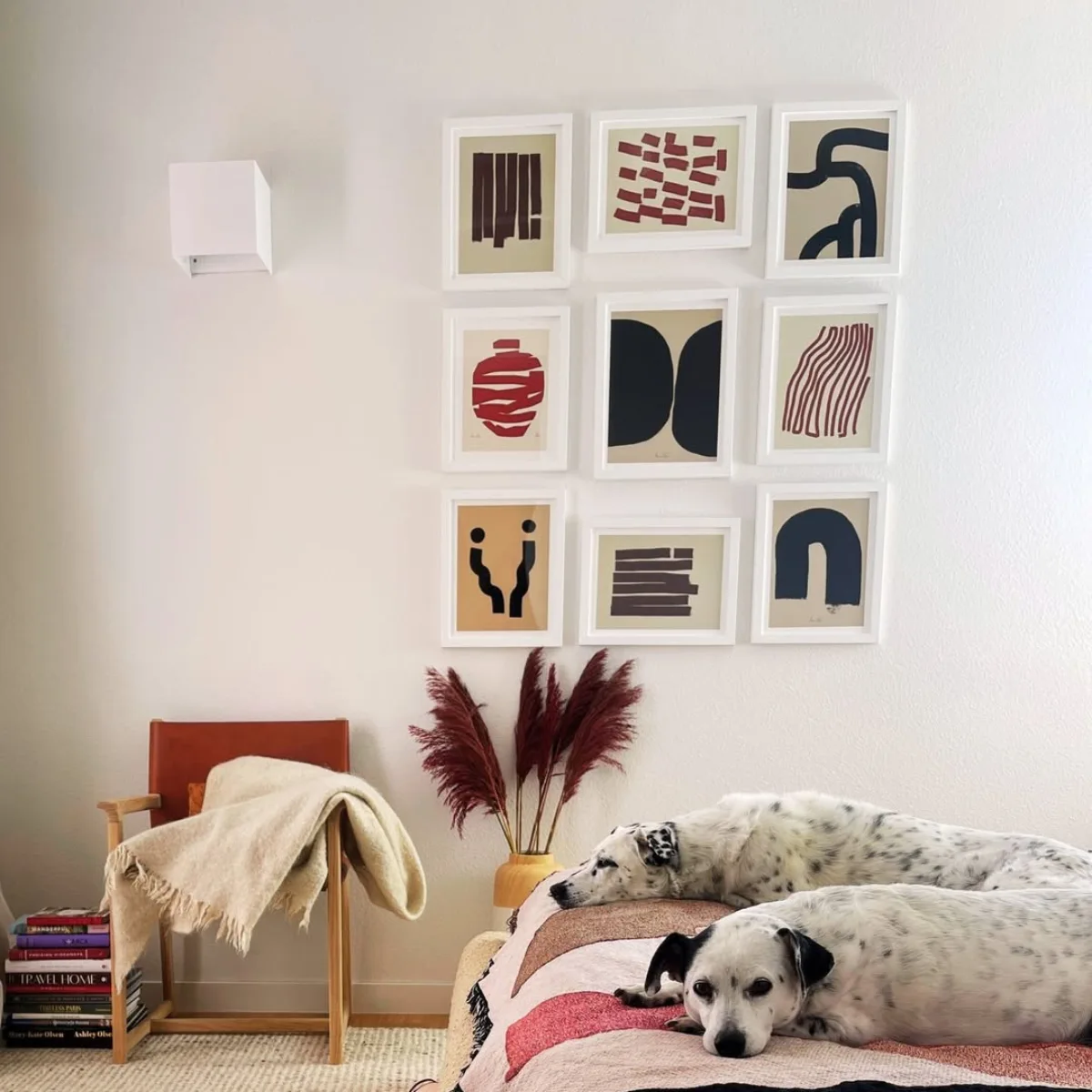 Dua ekor anjing dalmatian tidur di atas kasur berlatar gallery wall rapi berisi seni abstrak bernuansa merah bata dan hitam
