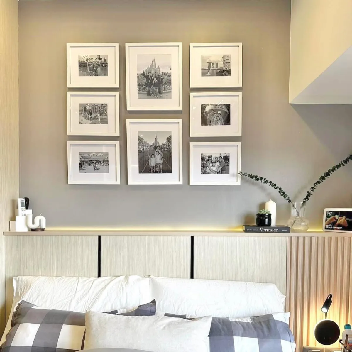 Dinding atas kasur dengan gallery wall simetris berisi kumpulan foto liburan keluarga hitam putih dalam bingkai putih tebal