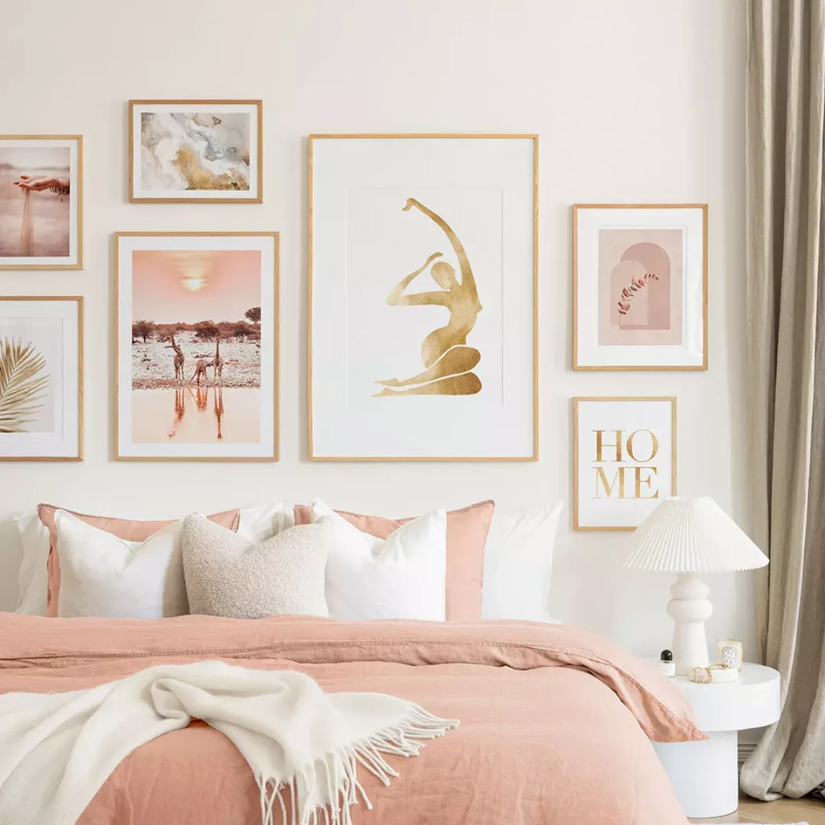 Dinding kamar bernuansa peach dengan susunan bingkai seni beraksen emas termasuk siluet tubuh wanita pemandangan savana dan tulisan home