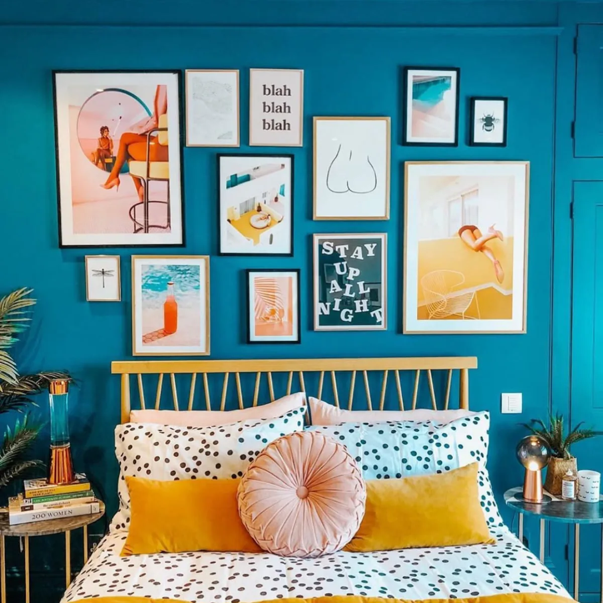 Dinding kamar berwarna biru cerah dengan galeri seni pop art yang penuh warna fotografi unik dan tipografi bertuliskan stay up all night