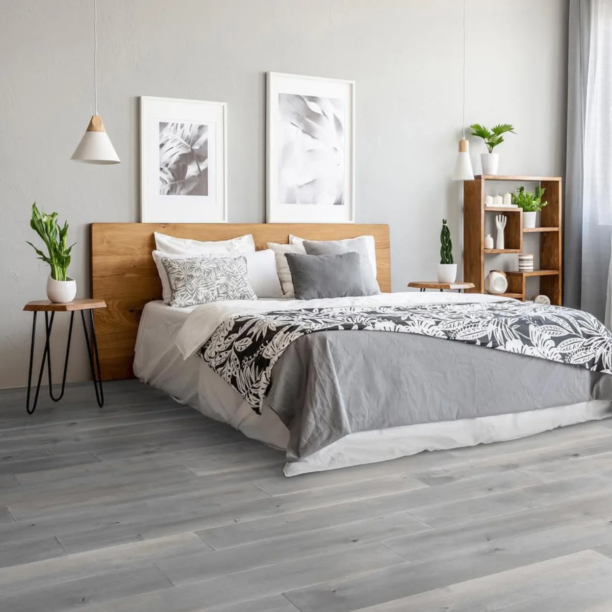 Kamar tidur kontemporer dengan lantai kayu parket abu-abu, headboard kayu solid lebar, rak pajangan kayu, dan tempat tidur dengan selimut bermotif daun tropis hitam putih.