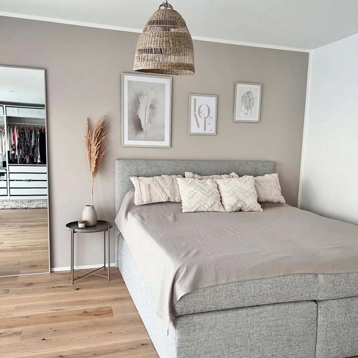Kamar tidur bergaya Scandinavian-Boho dengan dinding beige, lampu gantung rotan alami, cermin besar bersandar di dinding, dan dekorasi bunga kering pampas di samping tempat tidur.