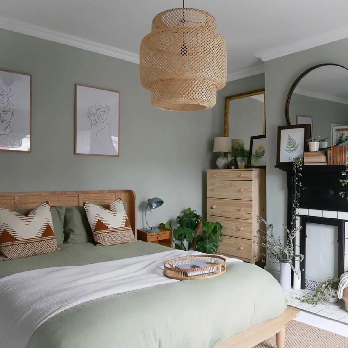 Kamar tidur bernuansa hijau sage natural (earthy tone) dengan lampu gantung bambu besar, headboard rotan, perapian dekoratif, dan cermin dinding berbentuk lengkung.