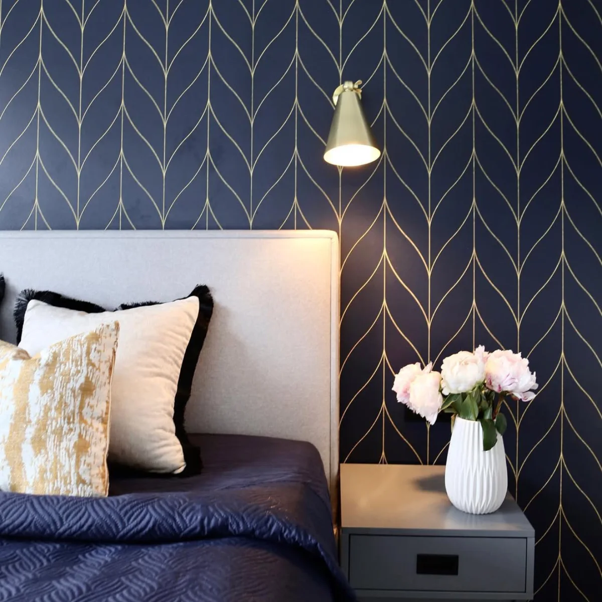 Interior kamar tidur mewah dengan wallpaper dinding warna biru navy motif garis emas geometris, lampu tidur gantung emas, dan bedding set biru senada.