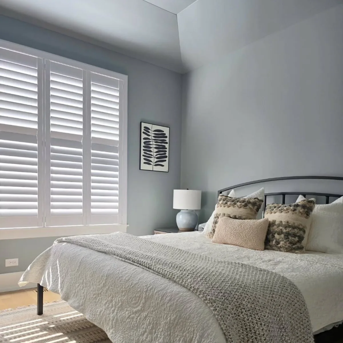 Suasana kamar tidur yang sejuk dan tenang dengan cat dinding warna abu-abu kebiruan (blue-grey), jendela besar berpenutup putih, dan tekstur selimut yang nyaman.