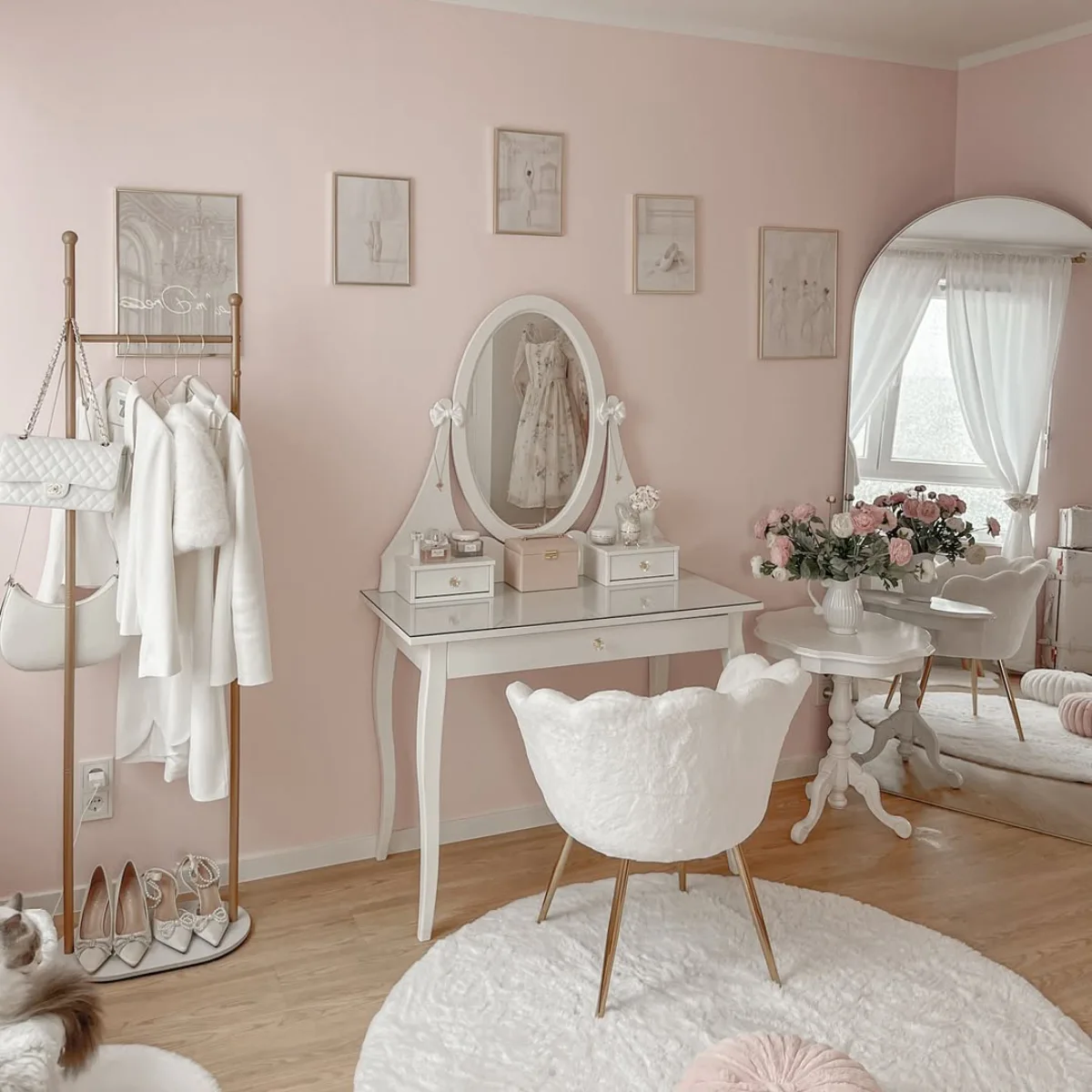 Kamar tidur wanita bergaya feminin dengan cat dinding full pink pastel, area meja rias putih klasik, dan dekorasi aesthetic yang manis.