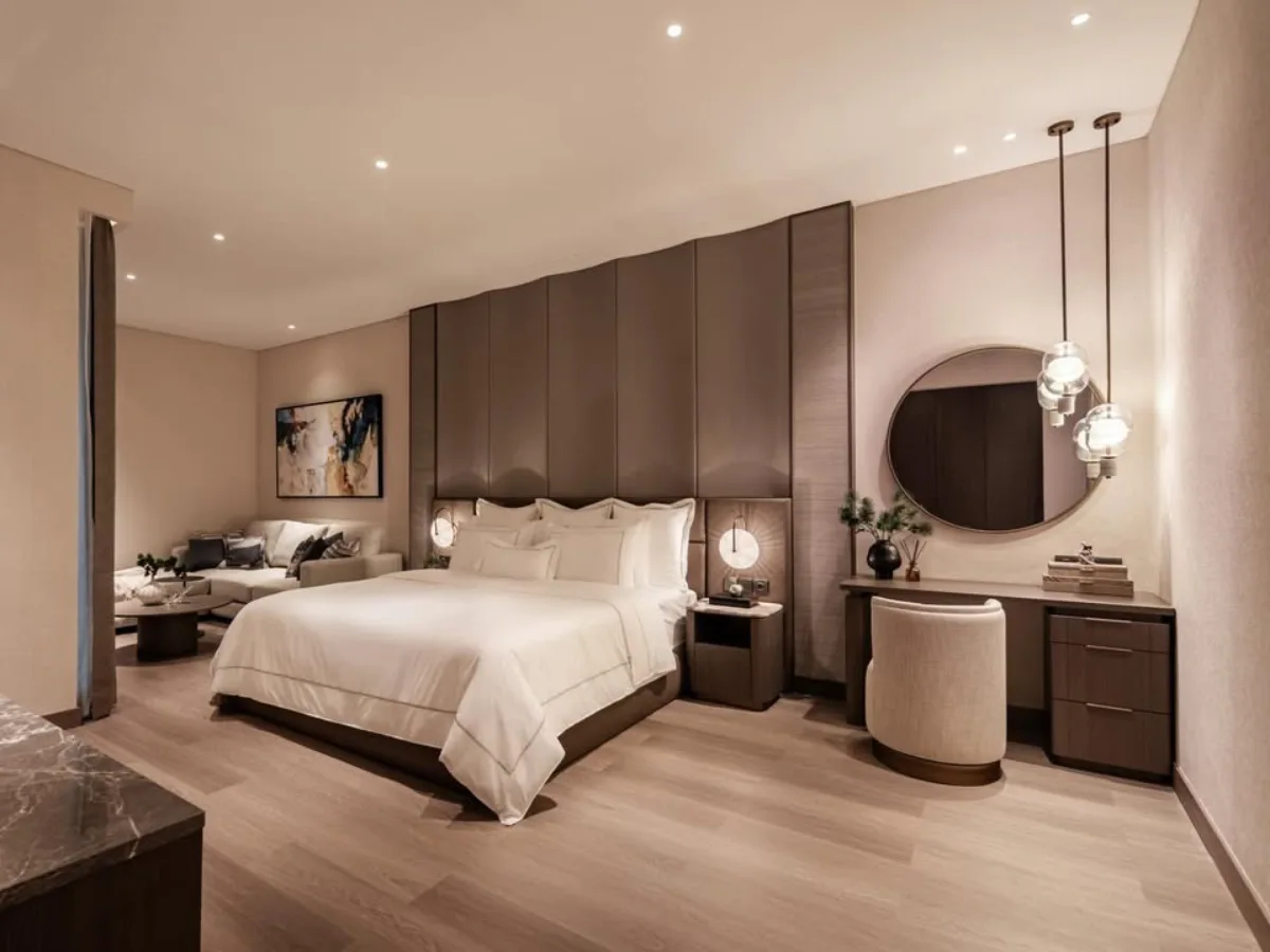 Kamar tidur modern kontemporer dengan nuansa warna taupe atau cokelat keabuan yang hangat, pencahayaan redup, dan dinding headboard yang empuk.