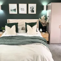 Kamar tidur dengan dinding hijau gelap bernuansa sejuk, tempat tidur putih minimalis, bantal hijau, dan pencahayaan lembut yang menenangkan
