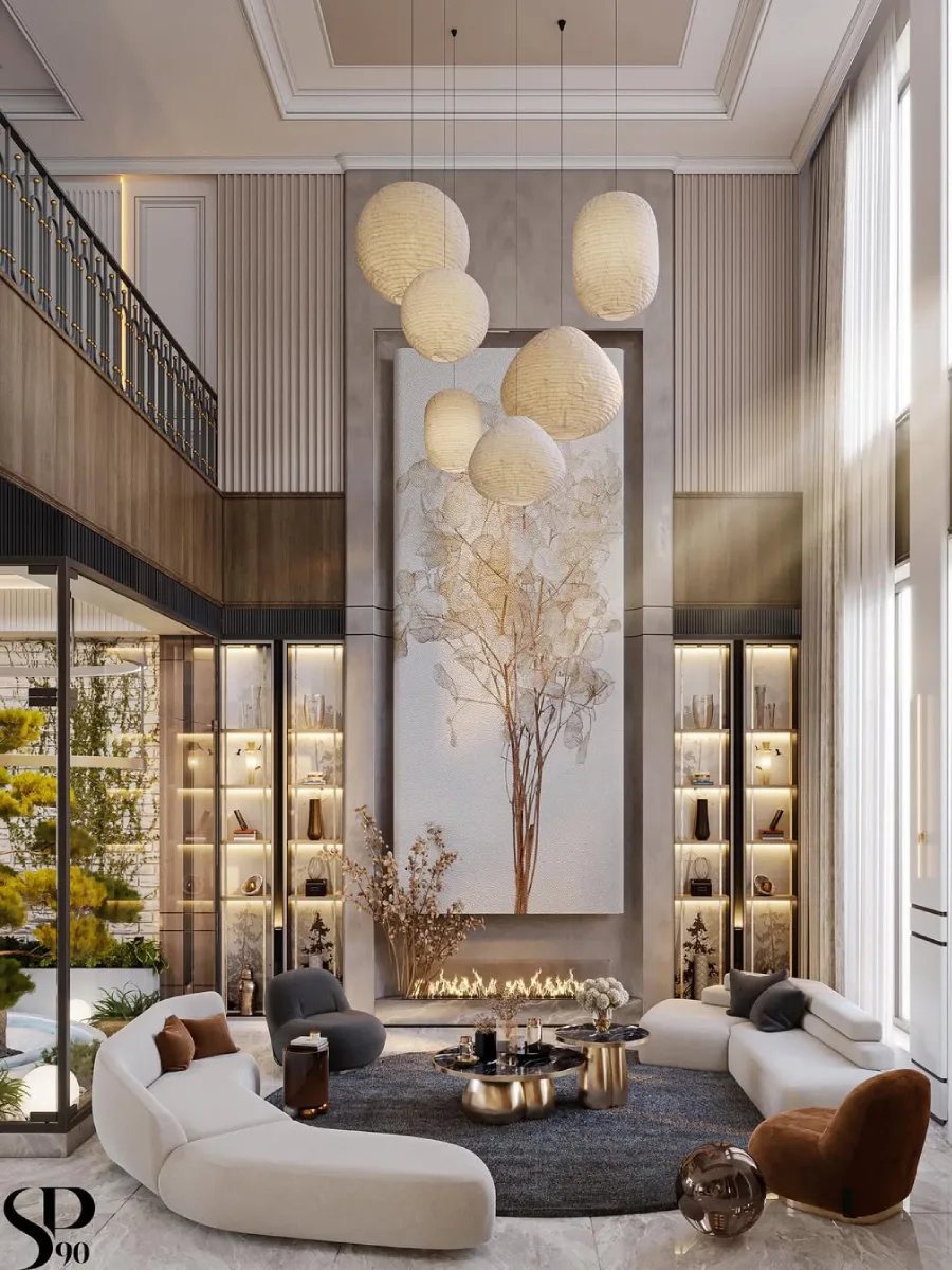 Ruang keluarga double-height yang elegan dengan dinding aksen lukisan pohon raksasa di atas perapian linear. Terlihat lampu gantung berbentuk bola kertas washi yang bertumpuk, sofa lengkung berwarna krem, dan rak pajangan tinggi dengan pencahayaan backlit yang hangat.