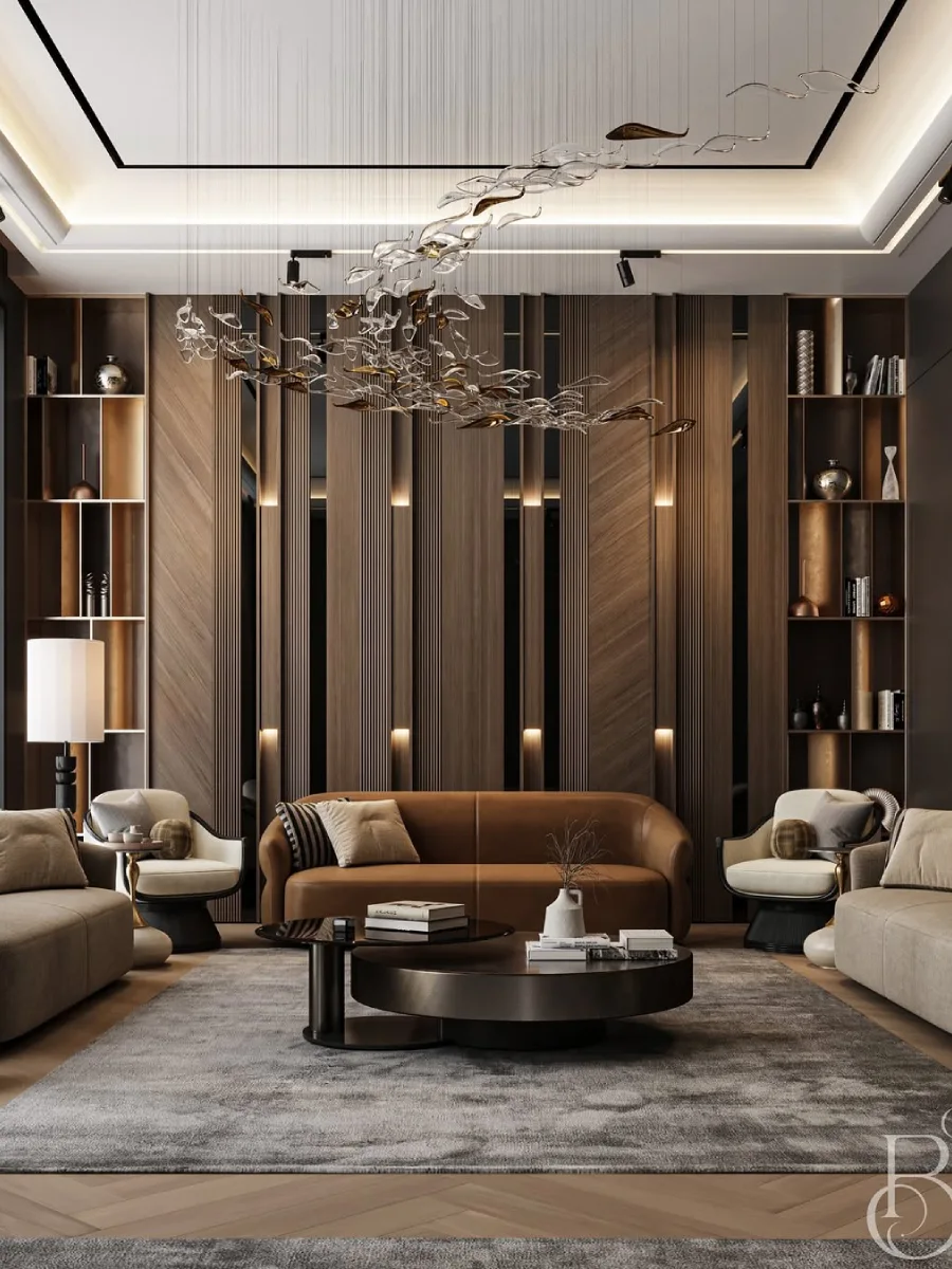 Ruang tamu kontemporer dengan simetri yang indah, menampilkan sofa kulit cokelat di tengah diapit oleh dua kursi lengan krem. Latar belakangnya adalah dinding kayu berpola chevron dengan rak buku terbuka di kedua sisi. Lampu gantung artistik berbentuk seperti instalasi kaca yang melayang menghiasi bagian tengah ruangan.