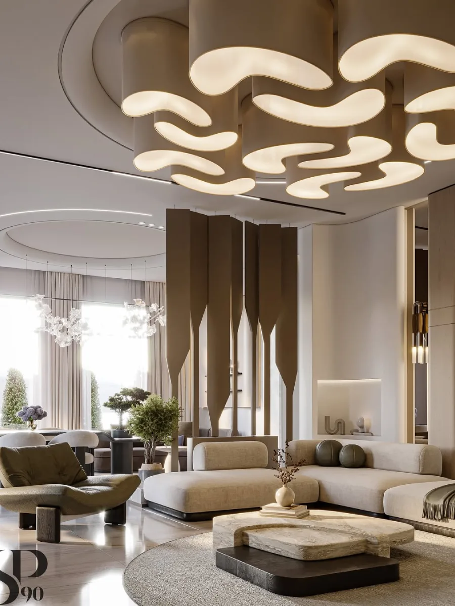 Sudut lain dari ruang keluarga bergaya organik yang memperlihatkan sekat ruangan berupa panel vertikal berwarna cokelat yang unik. Ruangan ini dipenuhi cahaya alami dari jendela besar di latar belakang, menciptakan suasana terang dan lapang pada furnitur minimalis berwarna netral.