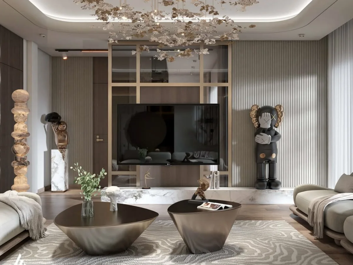 Area hiburan dalam ruang tamu mewah yang menampilkan TV layar datar terpasang pada panel dinding minimalis. Di sisi kanan, terdapat patung koleksi KAWS berukuran besar sebagai aksen seni modern. Ruangan ini menggunakan lantai kayu gelap, karpet bermotif tekstur tanah, dan meja kopi metalik. Dinding latar belakang memiliki tekstur garis vertikal (fluted wall) yang memberikan kesan tinggi dan elegan, diterangi oleh lampu gantung dekoratif yang menyerupai kelopak bunga emas.